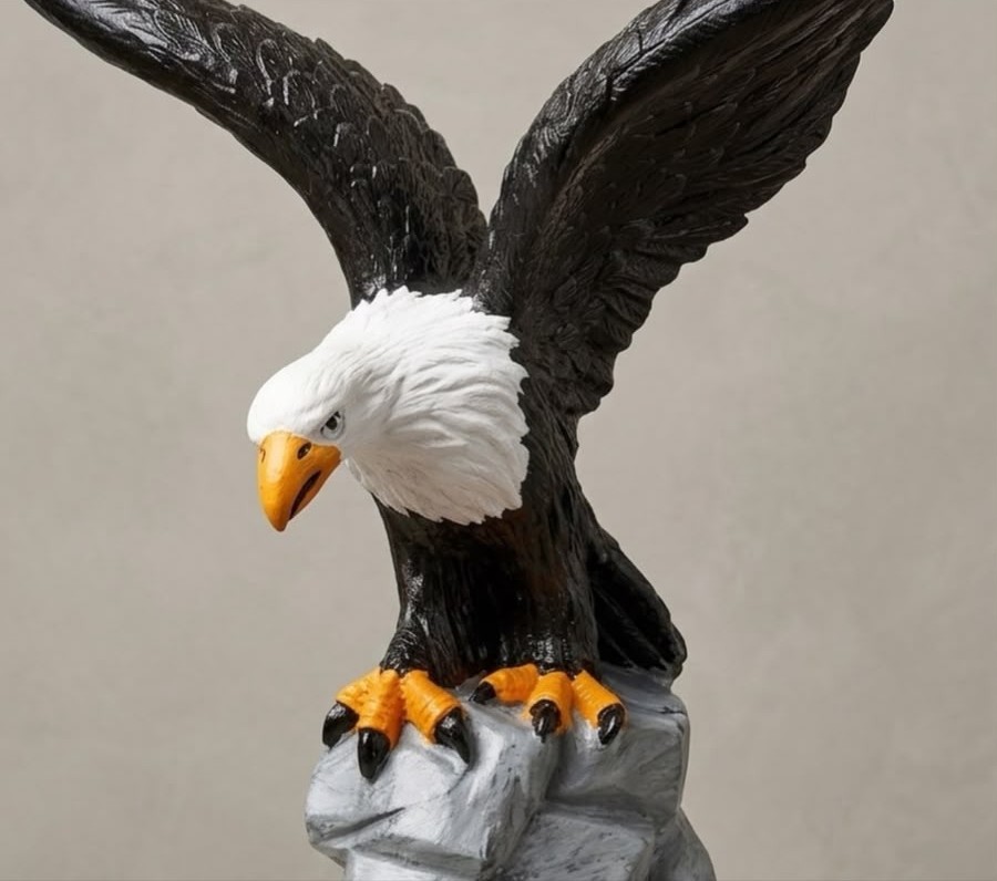 Escultura de águia com as asas abertas pousada sobre uma rocha, com corpo escuro e detalhes amarelos no bico e nas garras